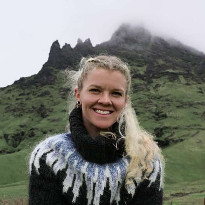 Creative director of Layover wearing Icelandic wool sweater posing in front rocky cliffs covered with green moss